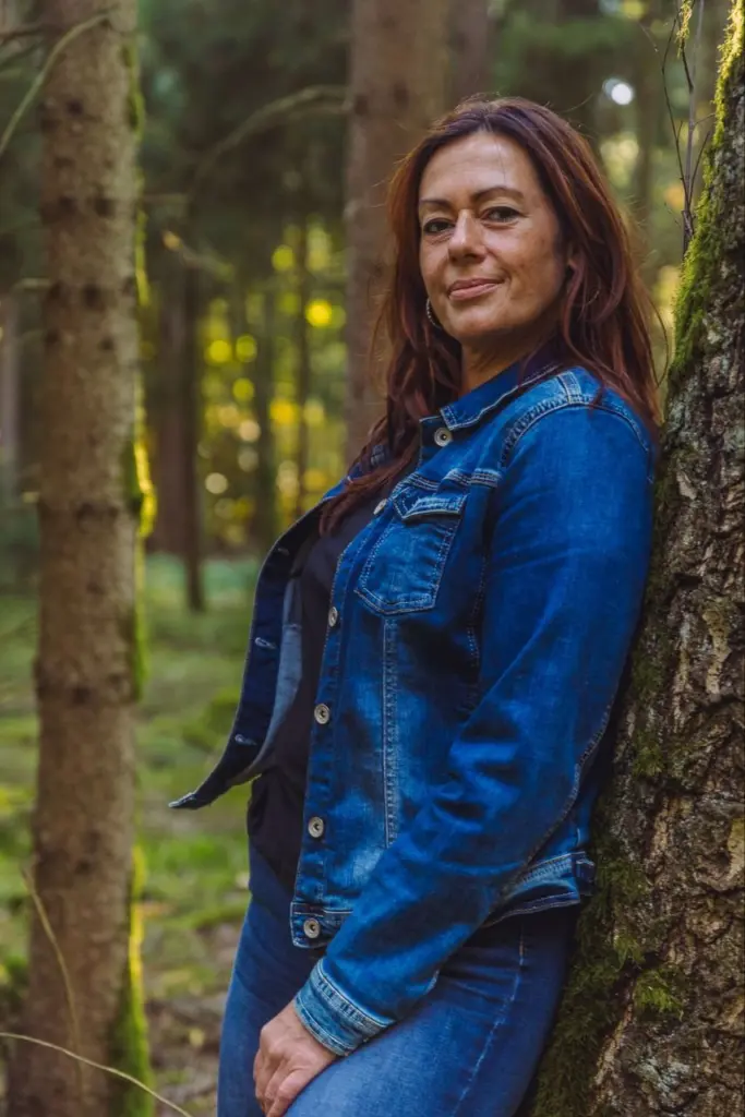 Katrin Iwicki lehnt im Wald an einem Baum und lächelt